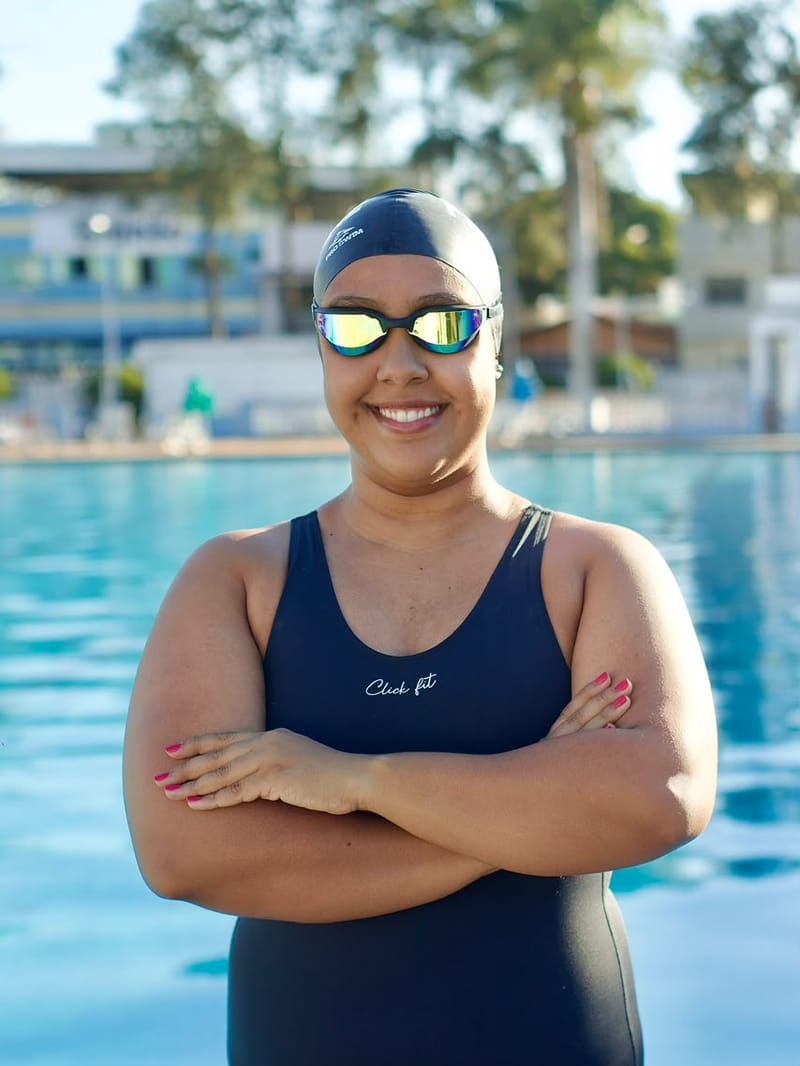 Personal de natação sorrindo de braços cruzados à beira da piscina