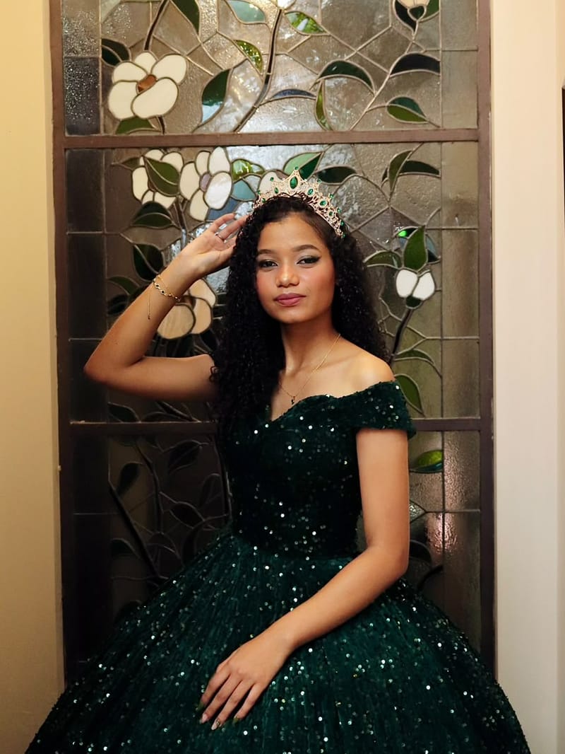 Debutante de vestido verde e coroa em frente a um vitral