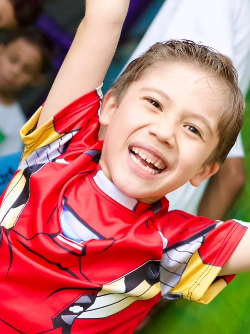 Menino com camiseta de super-herói sorrindo de braços abertos na festa