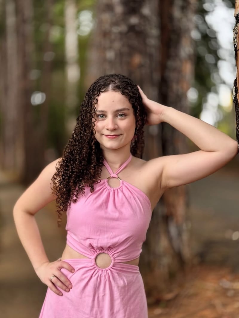 Jovem de vestido rosa e cabelo cacheado posando no bosque